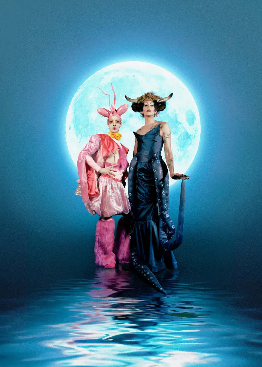 Soya the Cow und Piano Prince in schillernden Tierkostümen vor einem grossen Mond, der sich im Wasser spiegelt.
